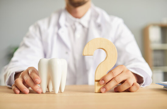 Professional dentist ready to answer all your questions about teeth health. Closeup male hands holding a white tooth model and a wooden question mark on the table. Dental care, stomatology concept