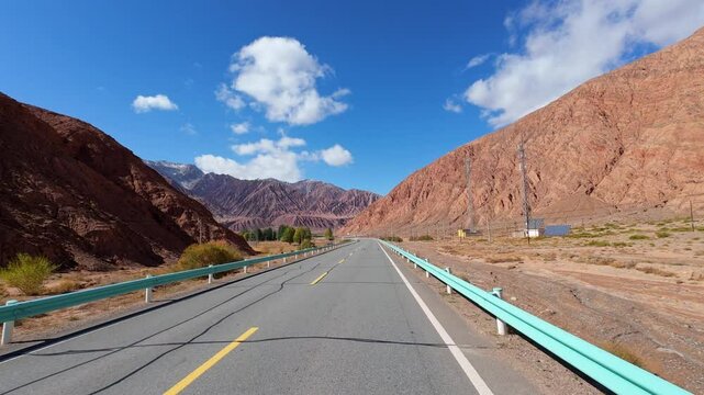 Driving on asphalt road passing through Gobi desert with colorful mountains on sunny autumn day in southern Xinjiang, China, POV from the car, 4k real time footage, travel concept.