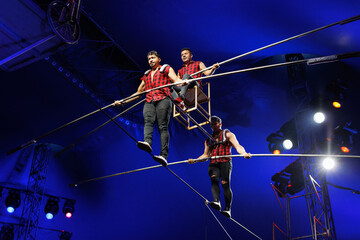 Aerial acrobats hold a rope with a chair on which a tightrope walker stands. A circus trick.