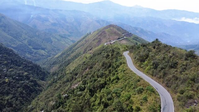 Drone flies along beautiful curvy road on lush green mountain, surrounded by valleys and mountain range between Guaranda and Montalvo, Bolivar Province, Ecuador