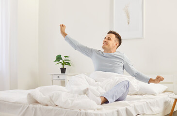 Young man who has had enough sleep wakes up in joyful mood in morning. Happy, smiling, well rested...