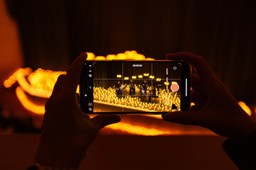 hands with phone taking video of symphonic orchestra on stage with lots of candles