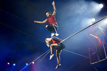 Acrobats tightrope walkers perform in a circus under the light of colorful spotlights. © Studio Peace