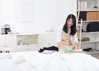 A young woman who works as a housekeeper picks up clothes from the bedroom and arranges them neatly.