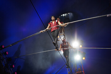Aerial acrobats hold a rope with a chair on which a tightrope walker stands. A circus trick. © Studio Peace