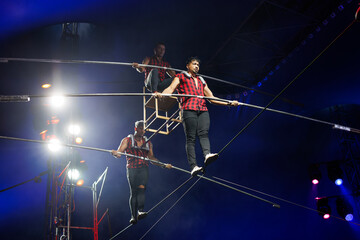 Aerial acrobats hold a rope with a chair on which a tightrope walker stands. A circus trick.