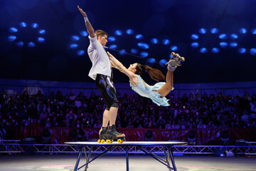 Young pair of acrobats, man and woman, on roller skates perform in a circus on a small round stage.