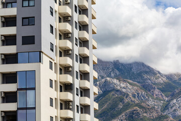 Modern apartment building with balconies and air conditioning units, set against a scenic mountain...