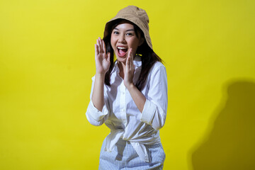 Asian woman enthusiastically calling out, wearing a beige bucket hat, white shirt, and striped...