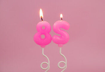 Pink air balloon shaped birthday candles burning on pink background. Number 85.