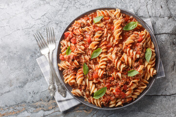 Italian fusilloni pasta or large fusilli with bolognese sauce close-up in a plate on the table. Horizontal top view from above