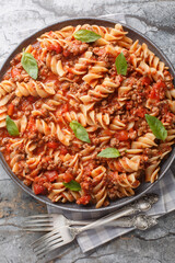 Fusilloni bolognese pasta with a hearty meat tomato sauce closeup on the plate on the table. Vertical top view from above