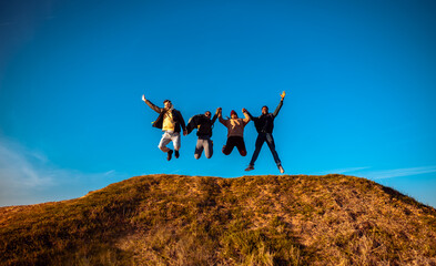 Smiling group of friends having fun jumping on top of the hill at sunset.