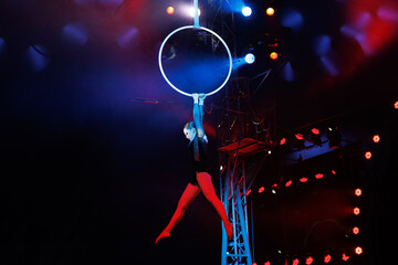 Aerialist performs on a gymnastic hoop under dome of the circus under the light of blue spotlights. © Studio Peace