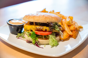 A juicy cheeseburger with lettuce, tomato, and sauce, served alongside seasoned fries on a white plate.