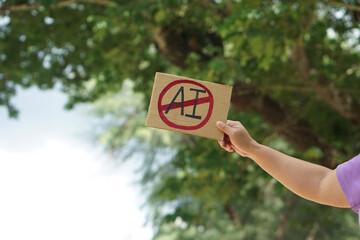 Close up hand holds paper card with No AI,  prohibition sign, outdoor nature background. Concept,...