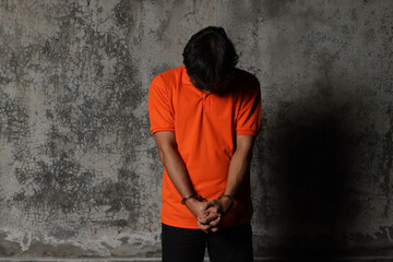 Arrested criminal suspect was wearing an orange shirt with his hands in handcuff, dramatic light...