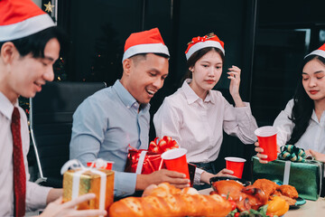 full length view of a group of business team wearing red Santa hat and exchange gift box together in the office for Christmas.