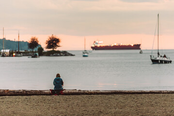 Lonely woman sitting on the beach, observing sunset in the ocean with couple boats on the horizon