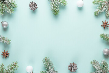 Christmas frame made of snowy fir branches, decorations, pine cones on pastel blue background. Flat lay. Happy New Year and winter holidays background. Top view with copy space