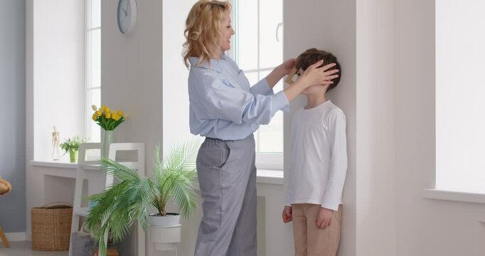 Mother measures the height of her child. Mom uses a set square ruler and a pencil to mark the height of her happy little son on a white wall at home. Growing up, development concept