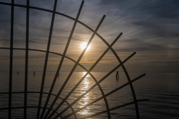 La silhouette di una  grata metallica a semicerchio con il mare sullo sfondo illuminato dalla luce del tramonto