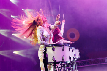 Group of female drummers in stage costumes in the circus arena in the light of spotlights and smoke.