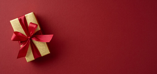 A beautifully wrapped gift box with a red ribbon lies on a rich red background, symbolizing celebration and festive cheer