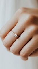 A close-up of a woman's hand showcasing an elegant engagement ring with a sparkling diamond, set against a dreamy blurred background