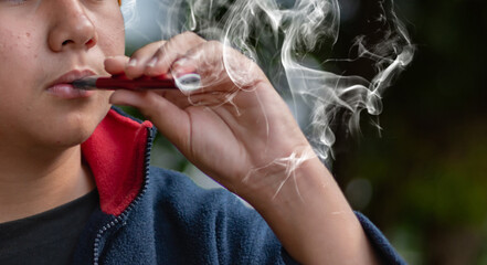 Closeup hand holding lighted e-cigarrette of schoolboy in private area, ideas for drug addiction of...