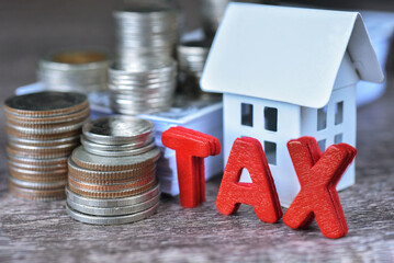 Stacking coins and red text "TAX" with white house and bundle of USD bill for property tax concept. The assessed value determine property tax rate.The tax time rolls arround each year for annual basis