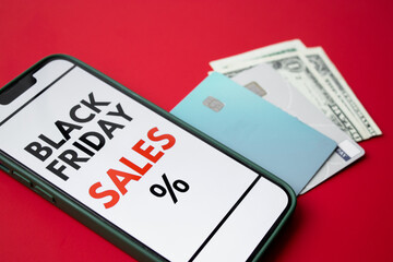Close up of a smartphone screen displaying a Black Friday online sale on red background with credit cards and money