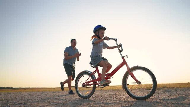 family play in the park. father teaching daughter to ride a bike. happy family kid dream concept. daughter learn to ride a bike sunset silhouette. father supporting child riding bike summer in park