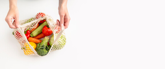 Female hands take out fresh vegetables from a bag on a white background. Top view, flat lay. Banner