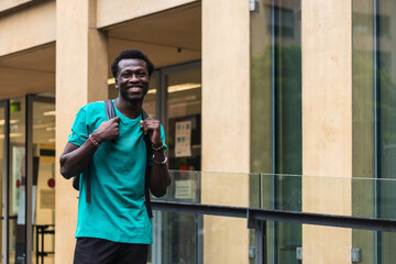 Smiling african american college student posing outside a classroom with his backpack