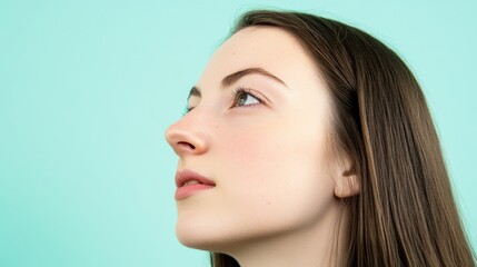 Fototapeta premium Profile of a young woman against a mint green background.