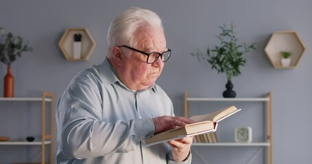 Concentrated and calm elderly man at home, enjoying domestic leisure time by reading a book or literature. Essence of relaxation from favorite hobby and the joy of reading at home library. - Powered by Adobe