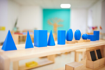 Montessori geometric solids in a preschool classroom. Bright blue shapes on wooden bases, including...