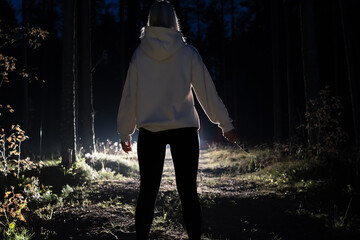 A maniac female with a knife in her hand in the night forest in front of a car with the headlights on. © Dmitri