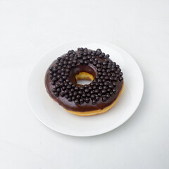A decadent chocolate donut garnished with small chocolate pearls, placed on a white dish. Great for culinary-focused visuals or dessert advertising.