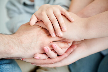 Cute family putting stacked hands together promising help and support to each other. Close up view of family members holding hands in supportive manner. Concept of unity, teamwork, mutual support.