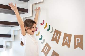 Preparation for the birthday. Girl hangs Happy Birthday sign on a wall.