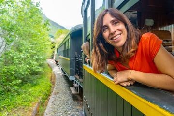 A woman is smiling and leaning out of a train window