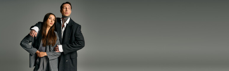 A fashionable duo stands side by side, showcasing their stylish outfits in a sleek environment.