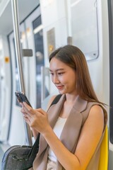 Young Asian Businesswoman Using Phone While Commuting In A Public Skytrain To Work 