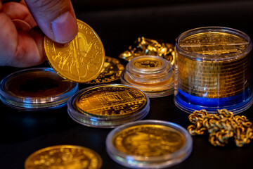 close-up hand fingers holding real austrian gold philharmonic coins in a black table with more golden coins and objects on it. investments, savings, finances stock photo