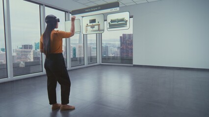 Asian female designer wearing virtual reality headset uses AI augmented reality interior design app to arrange office workspace or stylish apartment with 3D furniture and equipment. 3D visual effects.