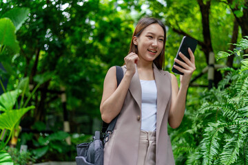 Asian Woman With Laptop Bag Using Phone Amid Greenery in A Park In the City