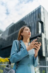 Fototapeta premium Asian Businesswoman Carrying Laptop Bag Using Phone In Front Of A Modern Office Building