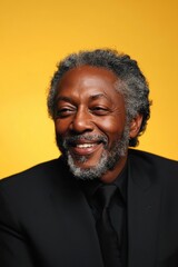 Elderly man smiling warmly in formal attire on yellow background